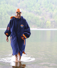 Load image into Gallery viewer, Female swimmer walking out of the water wearing Selkie recycled navy swim robe with orange fleece lining.